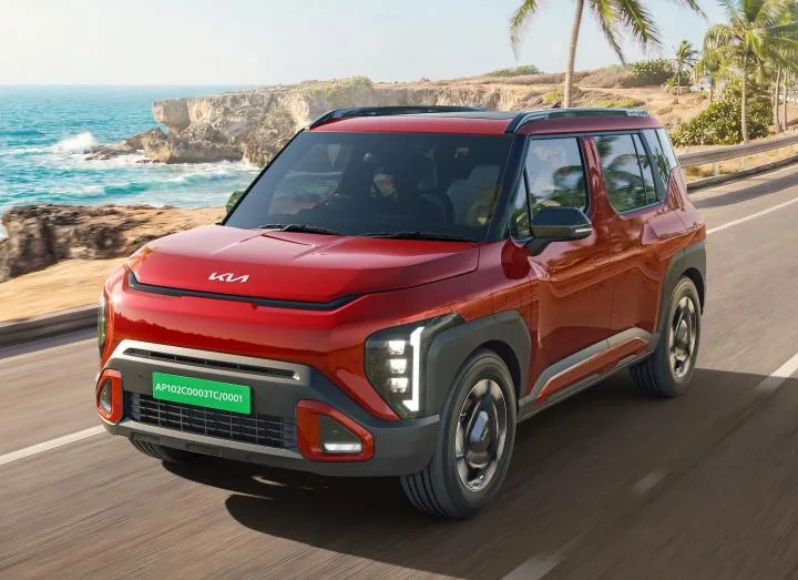 A red Kia Syros driving along a coastal road